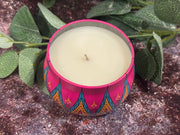 Candle in a colorful pink tin jar on a dark surface.