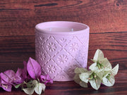 Pink concrete jar candle with decorative pattern.