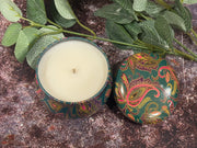 Candle in a decorative tin with paisley design on a textured surface 