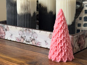 Pink textured candle shaped like a Christmas tree on a wooden surface.