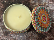 Candle in a decorative tin with a colorful lid on a textured surface