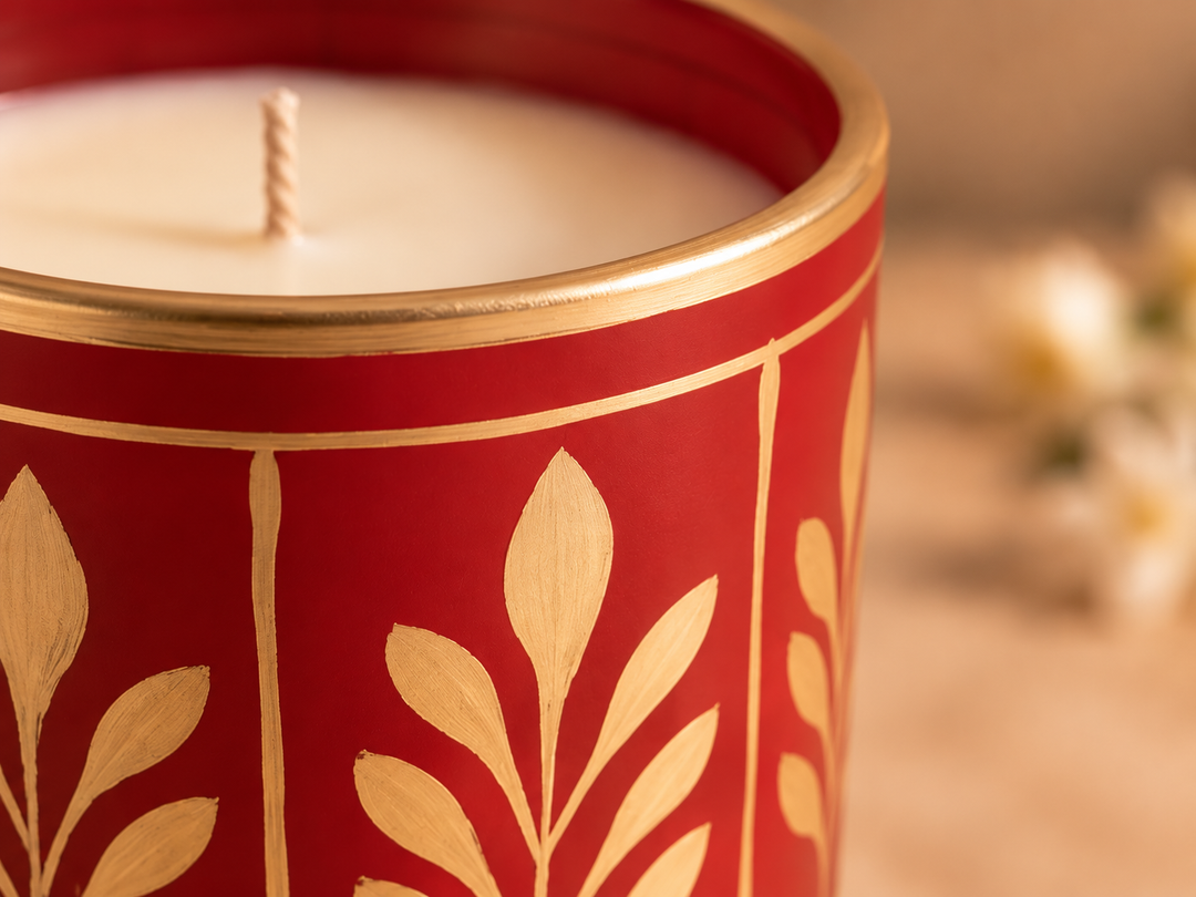 Close-up of the red scented candle showcasing its gold floral motif and metallic rim.